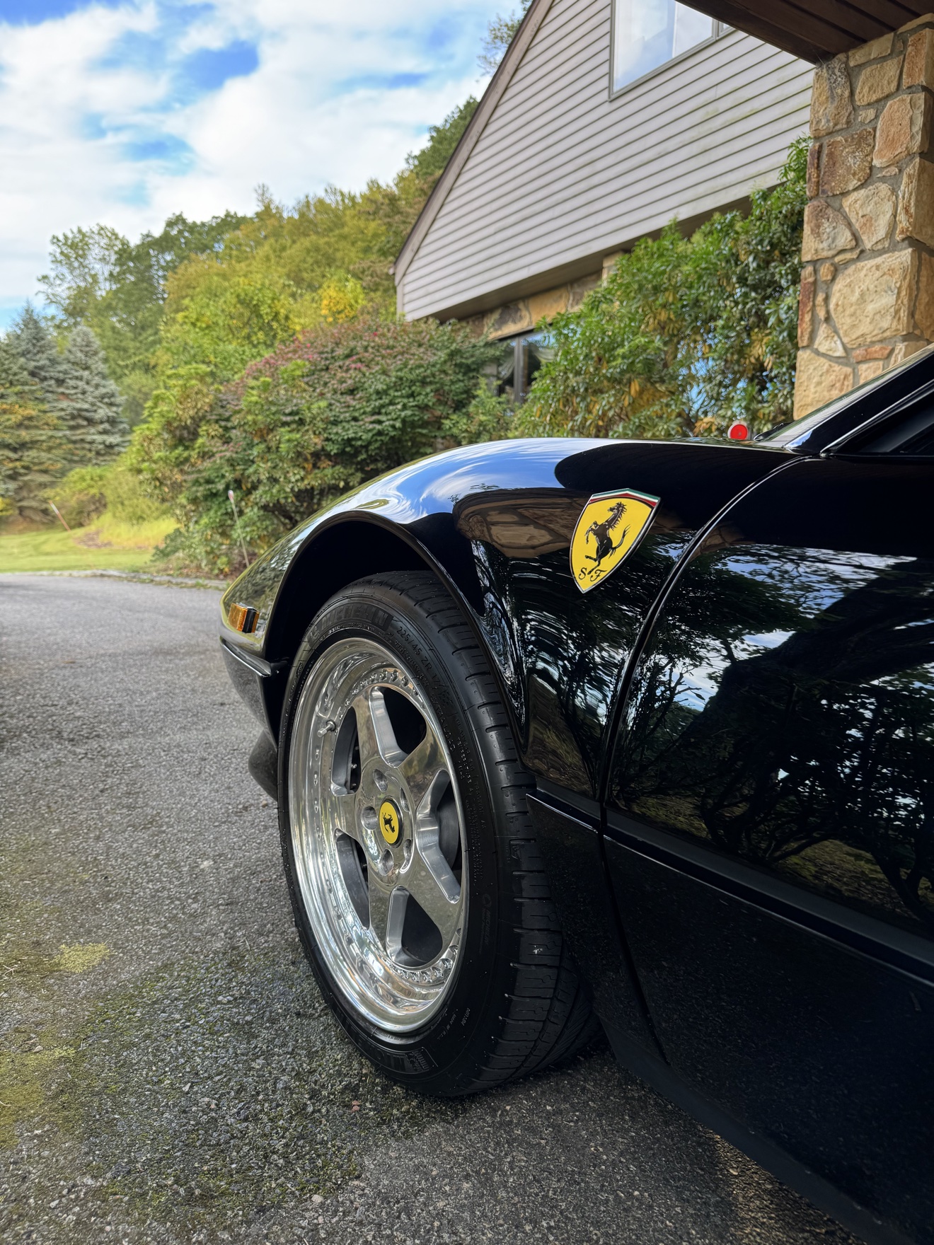 Close-up of the Ferrari badge on the front fender of a black 308 GTS with polished wheel