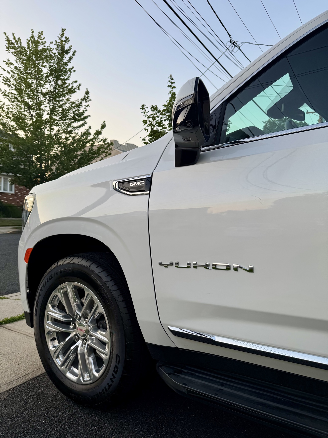 Close-up of the YUKON badge and chrome wheel on a white GMC Yukon SLT
