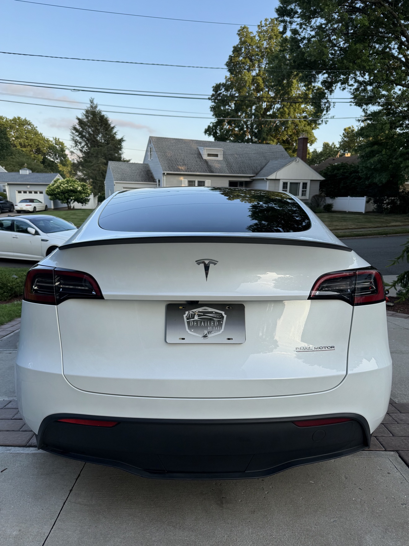 Rear view of a white Tesla Model Y with Dual Motor badge and Detailed by Yael plate frame